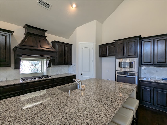 kitchen with light stone countertops, appliances with stainless steel finishes, premium range hood, a kitchen bar, and lofted ceiling