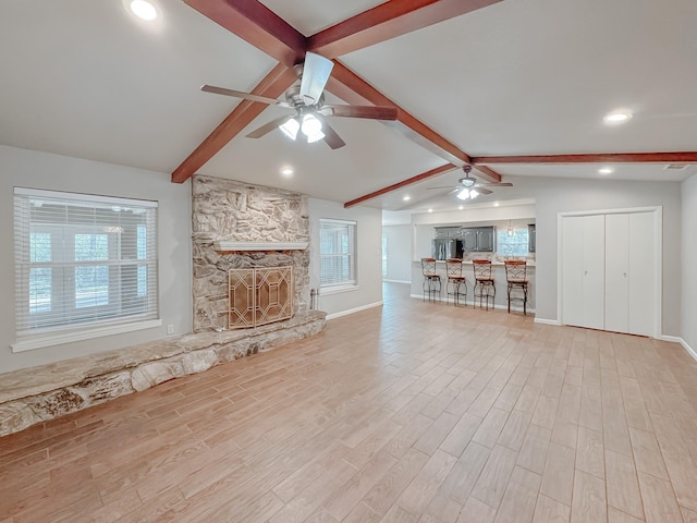 unfurnished living room with ceiling fan, vaulted ceiling with beams, a stone fireplace, and light hardwood / wood-style floors