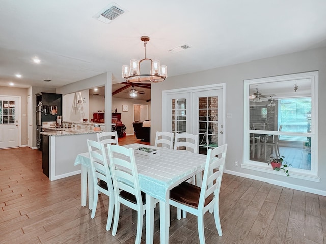 dining area with ceiling fan with notable chandelier and light hardwood / wood-style flooring