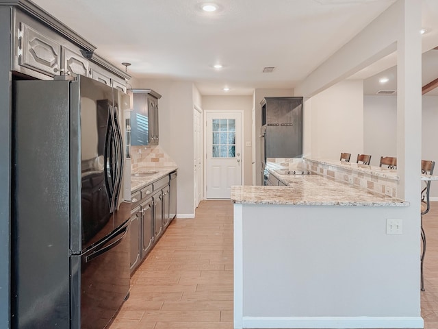 kitchen featuring black fridge, backsplash, kitchen peninsula, and gray cabinets