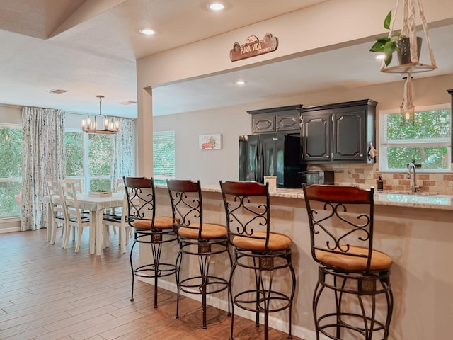 kitchen with decorative backsplash, black refrigerator, a breakfast bar, and an inviting chandelier