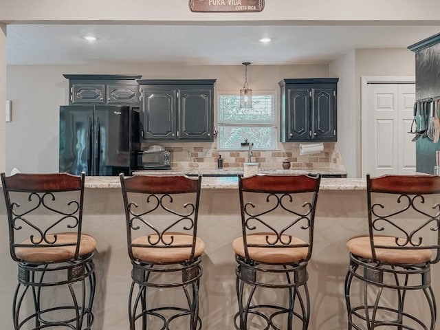 kitchen with light stone countertops, a kitchen island, black refrigerator, a kitchen breakfast bar, and backsplash