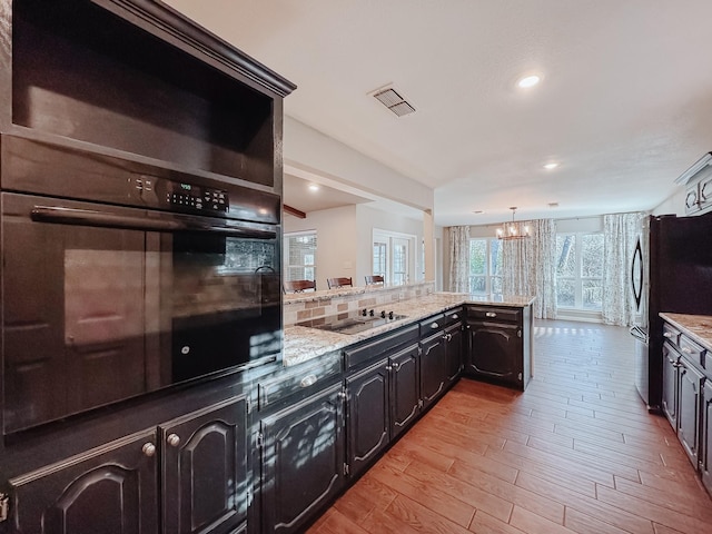 kitchen featuring pendant lighting, black appliances, tasteful backsplash, light stone counters, and light hardwood / wood-style flooring