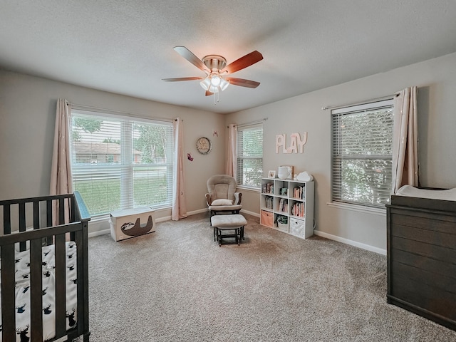 carpeted bedroom featuring ceiling fan, a nursery area, and a textured ceiling