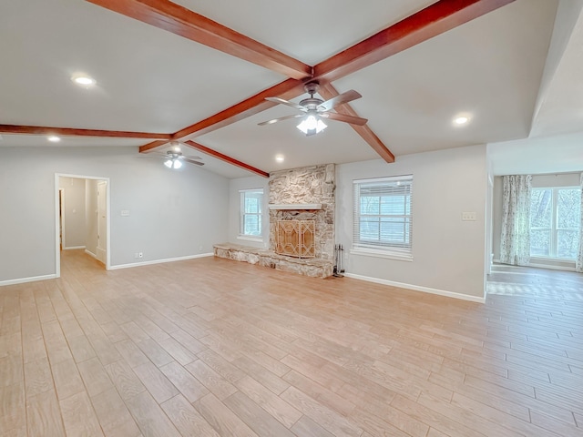 unfurnished living room with ceiling fan, light hardwood / wood-style flooring, a stone fireplace, and lofted ceiling with beams