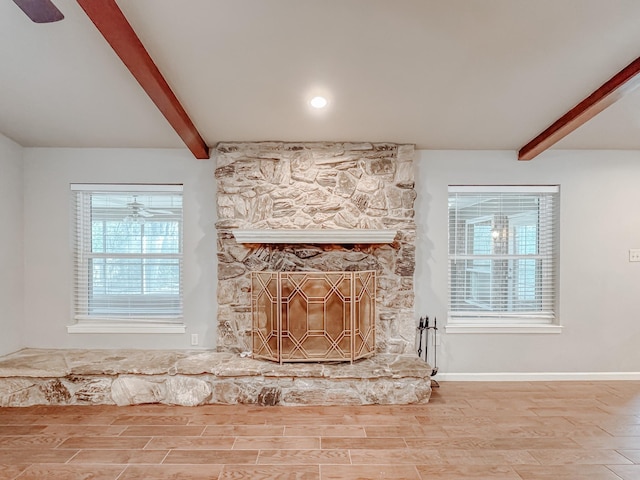 details with ceiling fan, beamed ceiling, a stone fireplace, and hardwood / wood-style floors