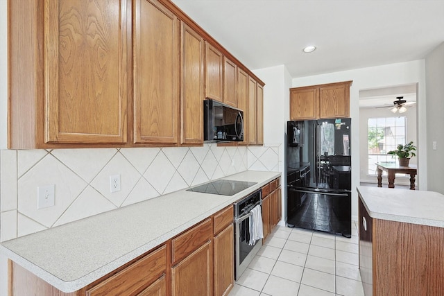 kitchen featuring light tile patterned floors, decorative backsplash, brown cabinetry, light countertops, and black appliances