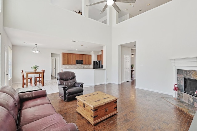 living room featuring wood finished floors, a tile fireplace, a ceiling fan, and baseboards