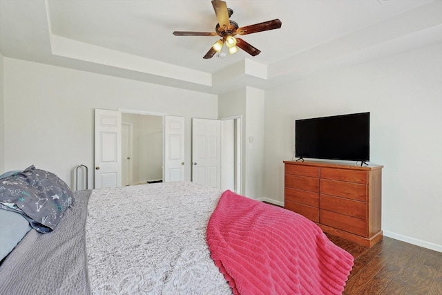 bedroom with a ceiling fan, a raised ceiling, baseboards, and wood finished floors