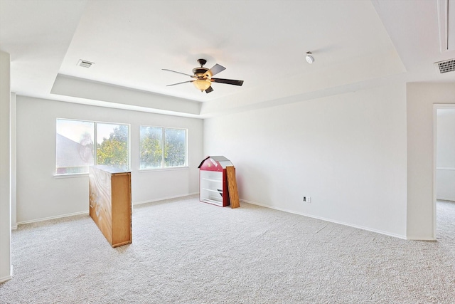 carpeted empty room featuring baseboards, a tray ceiling, and ceiling fan