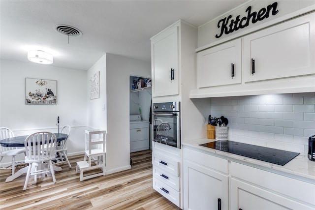 kitchen with light wood-type flooring, backsplash, oven, washer / dryer, and black electric cooktop