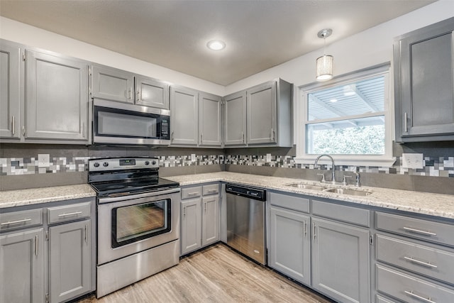 kitchen with appliances with stainless steel finishes, hanging light fixtures, decorative backsplash, gray cabinetry, and sink