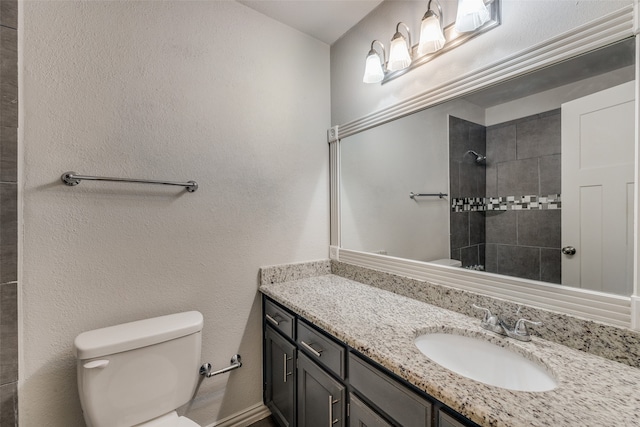 bathroom featuring a tile shower, vanity, and toilet