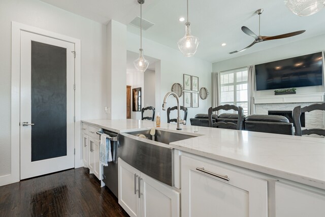 kitchen with pendant lighting, ceiling fan, dark hardwood / wood-style floors, a stone fireplace, and white cabinets