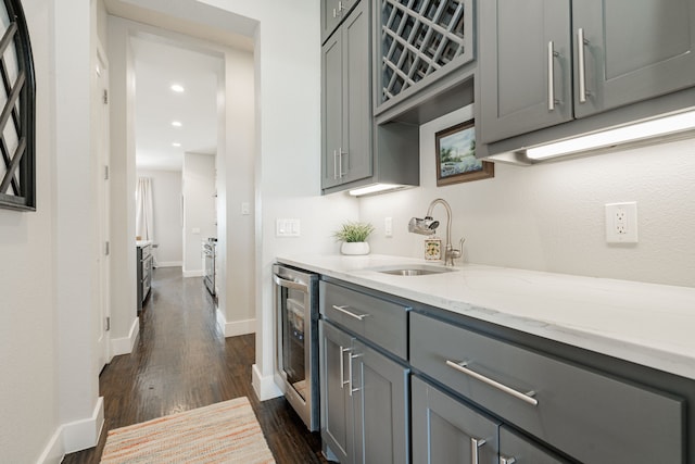 kitchen featuring gray cabinets, beverage cooler, sink, light stone countertops, and dark wood-type flooring