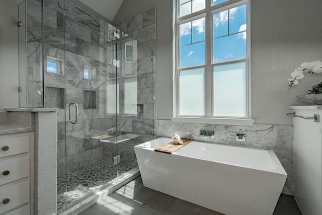 bathroom with plus walk in shower, tile patterned floors, vanity, lofted ceiling, and tile walls