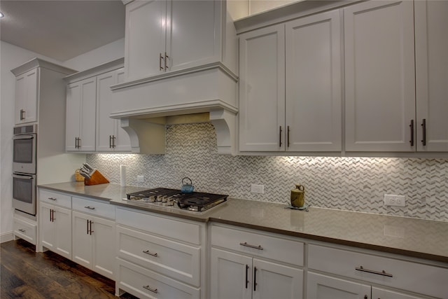 kitchen with backsplash, appliances with stainless steel finishes, white cabinetry, and dark hardwood / wood-style flooring