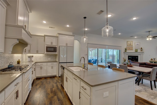 kitchen with an island with sink, appliances with stainless steel finishes, dark hardwood / wood-style floors, sink, and decorative light fixtures