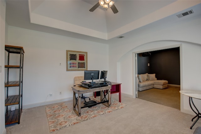 office space with light colored carpet, a tray ceiling, and ceiling fan