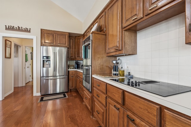 kitchen with dark wood-type flooring, lofted ceiling, stainless steel appliances, and decorative backsplash