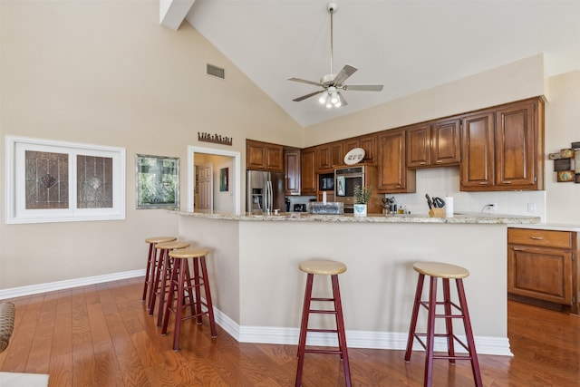 kitchen with dark wood-type flooring, stainless steel appliances, ceiling fan, and a breakfast bar