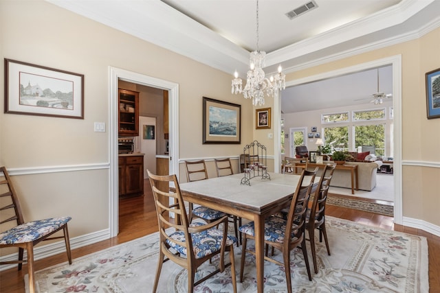 dining space featuring a tray ceiling, ornamental molding, ceiling fan with notable chandelier, and hardwood / wood-style flooring