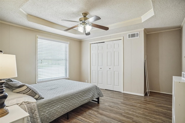 bedroom with a closet, a raised ceiling, dark wood-type flooring, ceiling fan, and ornamental molding