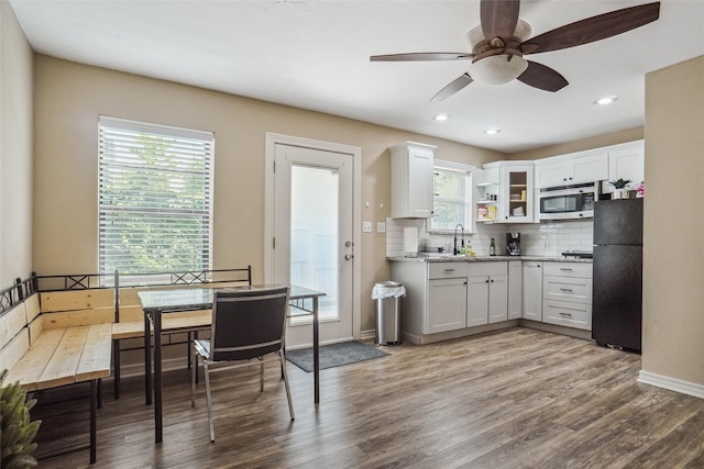 kitchen featuring a healthy amount of sunlight, hardwood / wood-style floors, white cabinets, and black fridge