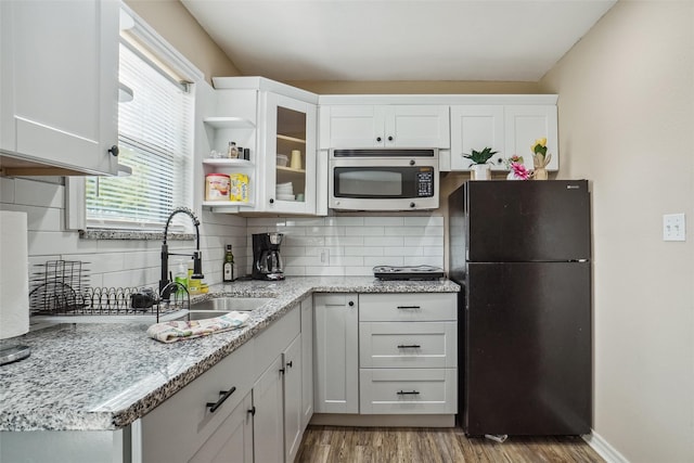 kitchen featuring black refrigerator, hardwood / wood-style floors, decorative backsplash, and white cabinetry