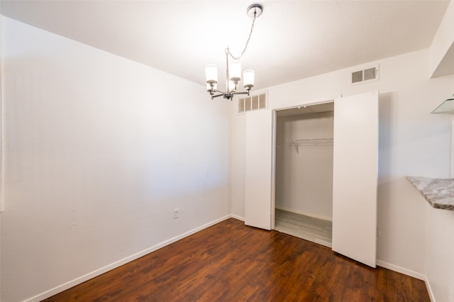 unfurnished bedroom featuring a closet, an inviting chandelier, and dark hardwood / wood-style floors