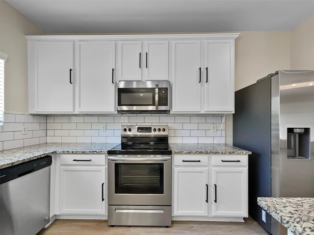 kitchen with light stone countertops, appliances with stainless steel finishes, light hardwood / wood-style floors, decorative backsplash, and white cabinetry