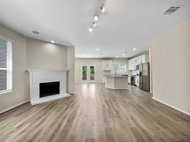 unfurnished living room with light wood-type flooring, sink, track lighting, and a brick fireplace