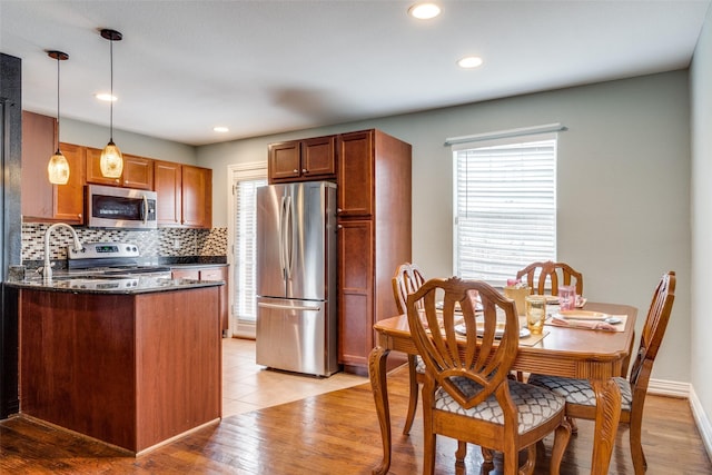 kitchen with kitchen peninsula, backsplash, stainless steel appliances, decorative light fixtures, and light hardwood / wood-style floors