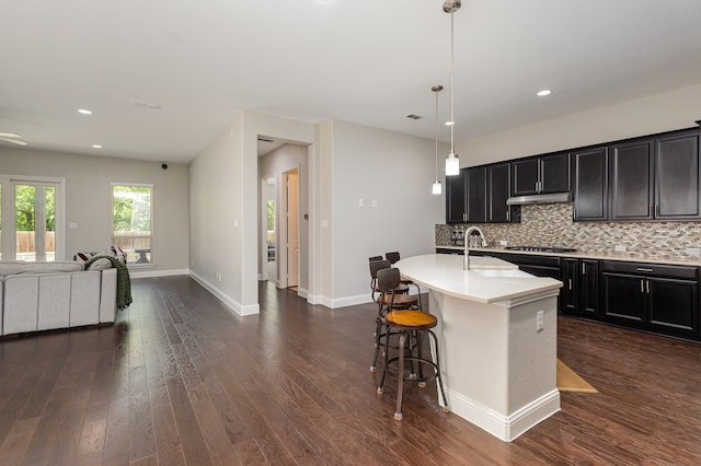 kitchen with a center island with sink, decorative light fixtures, a kitchen bar, sink, and dark wood-type flooring