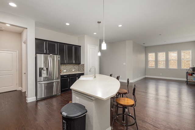 kitchen with a center island with sink, sink, stainless steel refrigerator with ice dispenser, decorative light fixtures, and dark wood-type flooring