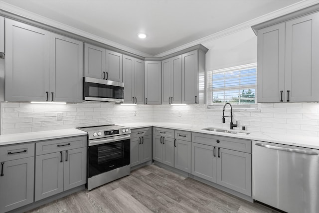 kitchen with sink, light hardwood / wood-style flooring, decorative backsplash, ornamental molding, and stainless steel appliances