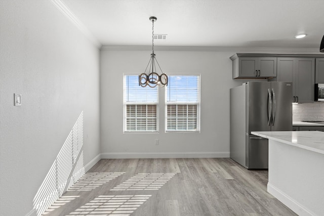 unfurnished dining area featuring crown molding, a chandelier, and light wood-type flooring