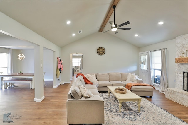 living room featuring a wealth of natural light, a stone fireplace, beam ceiling, and hardwood / wood-style flooring