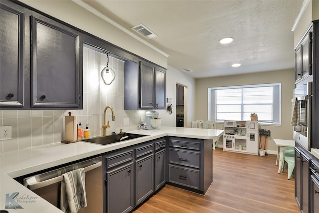 kitchen with backsplash, a textured ceiling, light hardwood / wood-style flooring, sink, and stainless steel dishwasher