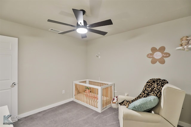 carpeted bedroom featuring a nursery area and ceiling fan