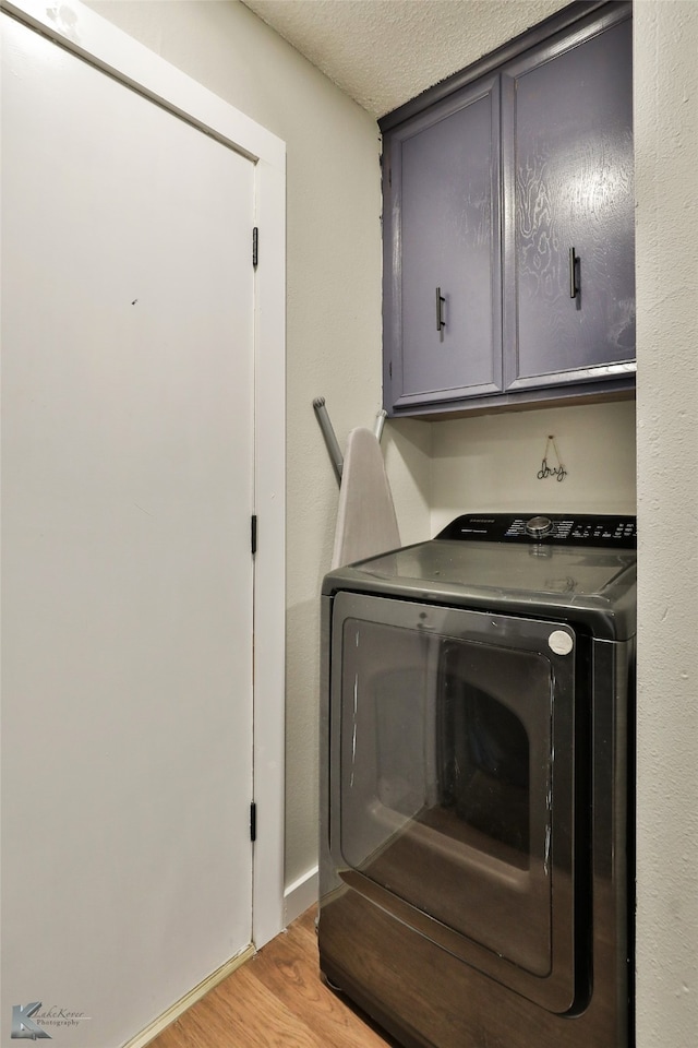 laundry room featuring washer / clothes dryer, a textured ceiling, cabinets, and light hardwood / wood-style flooring