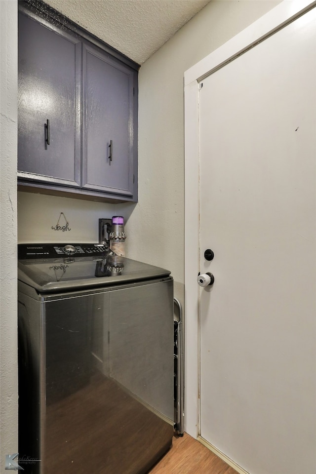 laundry room featuring washer / clothes dryer, cabinets, light hardwood / wood-style flooring, and a textured ceiling