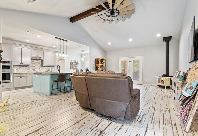 living room with french doors, a wood stove, lofted ceiling with beams, and light hardwood / wood-style flooring