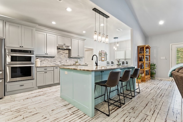 kitchen featuring decorative light fixtures, a kitchen breakfast bar, double oven, lofted ceiling, and a center island with sink