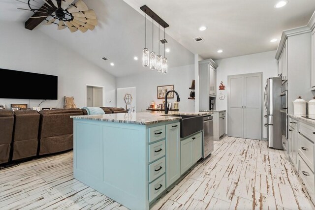 kitchen featuring a kitchen island with sink, pendant lighting, stainless steel refrigerator, light stone countertops, and ceiling fan