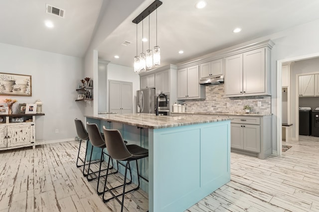 kitchen featuring stainless steel refrigerator, decorative light fixtures, washer and dryer, decorative backsplash, and a breakfast bar