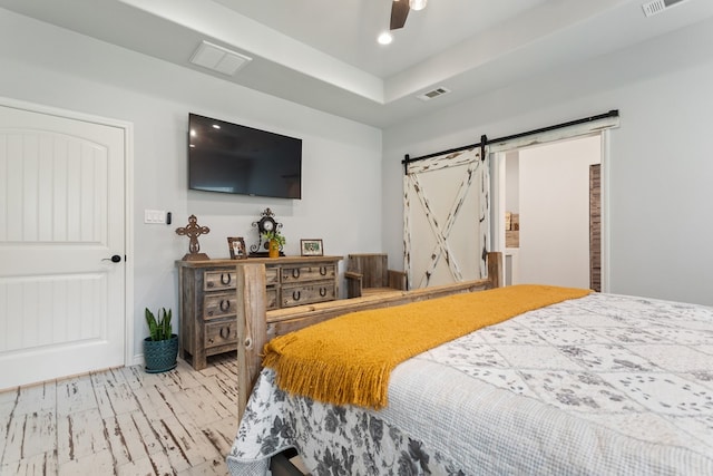 bedroom with ceiling fan, a barn door, and light hardwood / wood-style floors