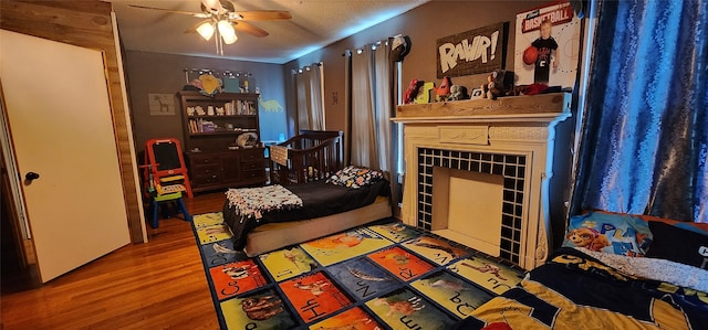 interior space with wood-type flooring, a tiled fireplace, a textured ceiling, and ceiling fan