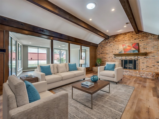 living room featuring brick wall, light hardwood / wood-style floors, vaulted ceiling with beams, and a fireplace