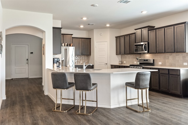 kitchen featuring appliances with stainless steel finishes, dark hardwood / wood-style floors, decorative backsplash, and a breakfast bar area